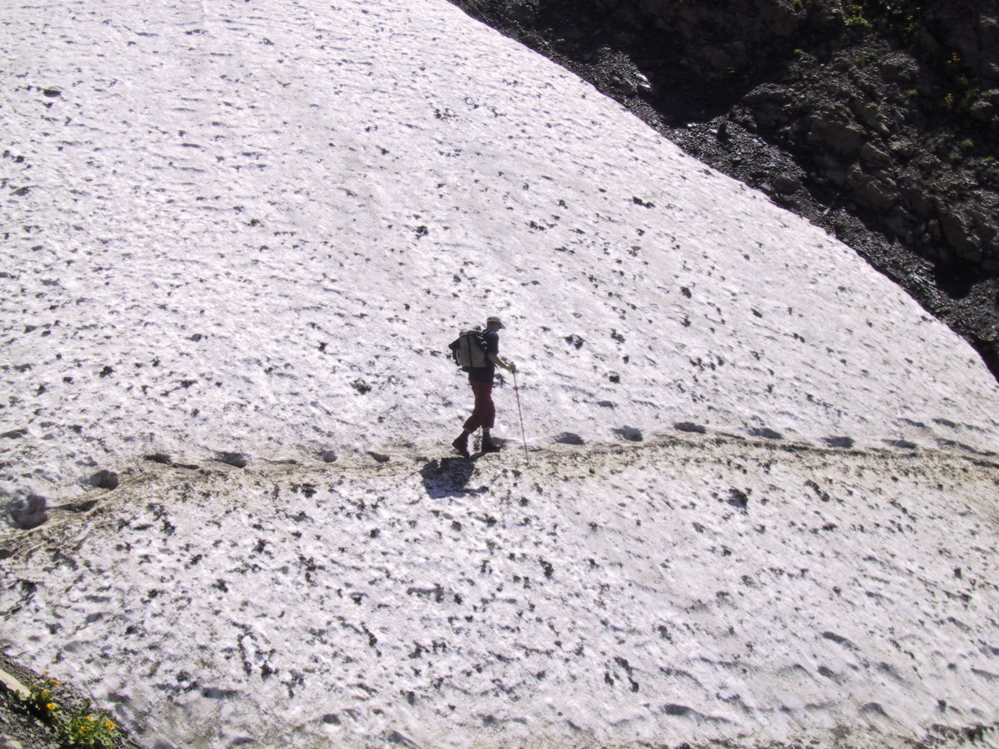 Wanderin quert ein steiles Altschneefeld auf schmaler Spur